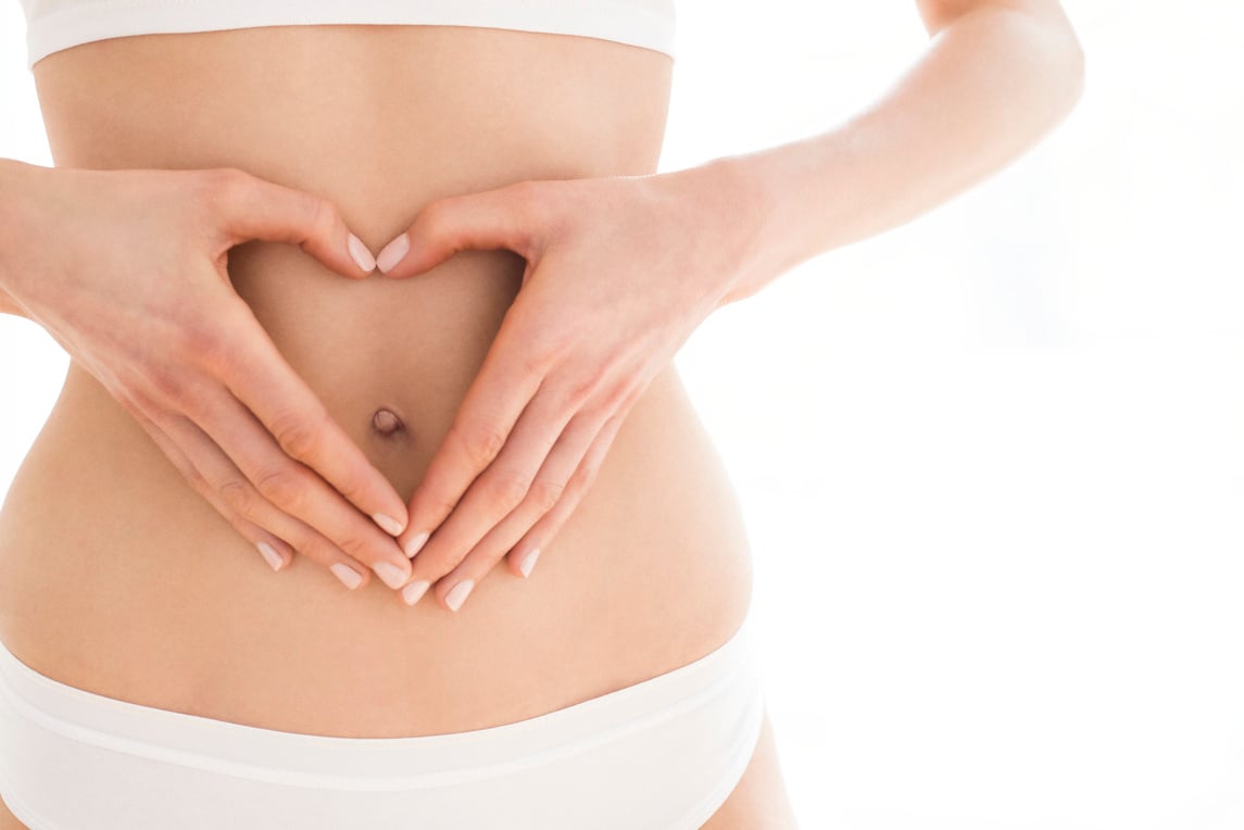 Young woman with hands in heart shape around navel.